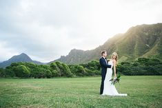 a bride and groom standing in the grass with mountains in the background at their wedding