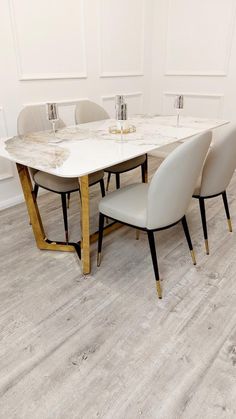 a white marble dining table with four beige chairs and two silver candlesticks on each side