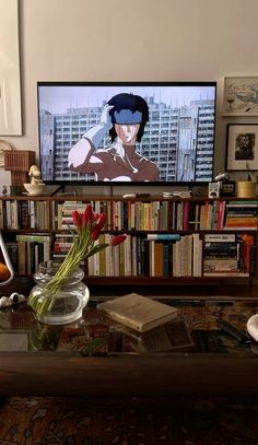 there is a vase with flowers in front of a television screen and bookshelves