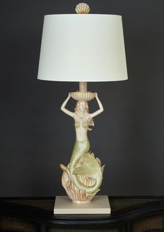 a table lamp with a mermaid figurine on it and a white shade over the base