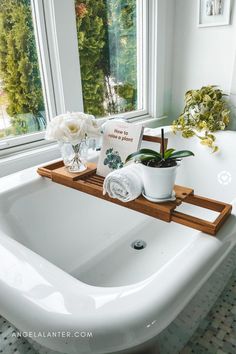 a white bath tub sitting under a window next to a potted plant and flowers