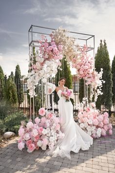 a woman in a wedding dress standing under a floral arch with pink and white flowers