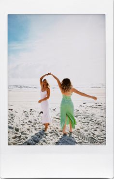 two women standing on the beach with their arms in the air