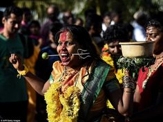 a woman in yellow and green dress holding a pot on her head with other people behind her