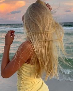 a woman standing on top of a sandy beach next to the ocean with her hair blowing in the wind