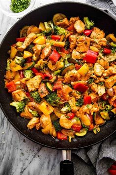 a skillet filled with chicken and veggies on top of a marble counter