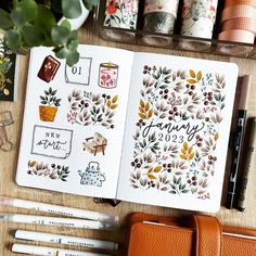 an open planner book sitting on top of a wooden table next to markers and pens