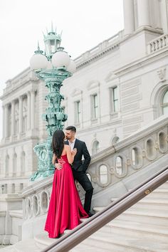 a man and woman in formal wear standing on steps next to a light pole with a fountain behind them