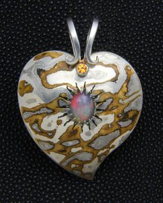 This heart pendant is made from Mokume Gane, a process of metal fabrication that dates back to the age of the Samurai. It involves fusing two or more alloys that are then carved, twisted, sanded, or otherwise manipulated to produce a pattern similar to wood grain. In this case, the metals I used were sterling silver, brass, and a Japanese alloy called Shibuichi. In the center, as though bursting from a volcano, is an African Welo Opal. The accent stone at the top, beneath the scrolls in the bail, is a faceted citrine. The pendant measures 2 inches from the tip to the top of the bail. Artisan Heart-shaped Jewelry For Anniversary, Silver Hand Forged Heart Necklace, Hand Forged Silver Heart Necklace, Artisan Heart Pendant Jewelry, Silver Heart Necklace, Hand Forged, Artistic Heart-shaped Sterling Silver Jewelry, Unique Hand Forged Heart Pendant, Unique Hand Forged Heart Pendant Jewelry, Artisan Carved Jewelry For Anniversary