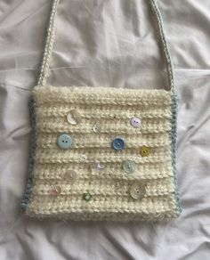 a crocheted purse with buttons on it laying on top of a white sheet