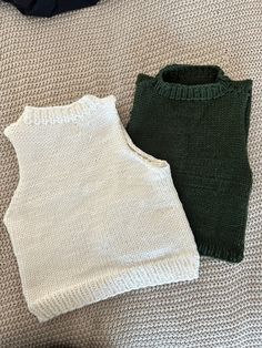 two sweaters sitting on top of a bed next to each other, one green and the other white