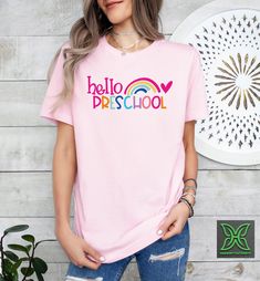 a woman wearing a pink t - shirt with the word hello preschool in rainbow letters