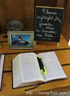 an open book sitting on top of a wooden table next to two framed pictures and a pen