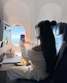 a woman sitting on an airplane looking at her cell phone with headphones in her ears