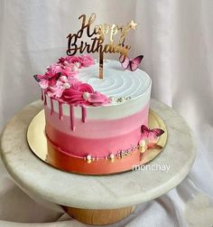 a birthday cake with pink flowers and butterflies on top is sitting on a white table