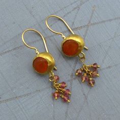 "A whimsical design gives this Garnet gold earrings an air of playfulness. An orange Carnelian gemstone serves as the centerpiece, wrapped with 22k solid gold combined with pink Tourmaline beads hanging on 14k gold chain and 22k gold wire that dangle freely for eye-catching movement. The back of these earrings made of 9k solid gold Handmade 14k yellow gold locking French wires. ~ Earrings width - 0.4'' ( 11 mm). ~ Length without the ear wire - 1\" (26 mm). ~ Length from top of the ear wire to bo 22k Gold Earrings, Carnelian Earrings, Orange Carnelian, Garnet And Gold, Gold Dangle Earrings, Ruby Pendant, Tourmaline Beads, Whimsical Design, Ruby Earrings