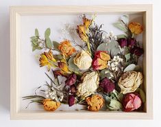 an arrangement of dried flowers is displayed in a wooden frame on a white wall background