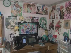 a desk with a computer and many anime pictures on the wall