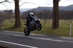 a person riding a motorcycle on the road near some trees and grass with mountains in the background