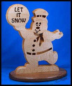 a wooden snowman figurine holding a sign that says, let it snow