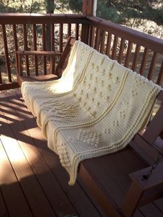 a white crocheted blanket sitting on top of a wooden porch next to a bench