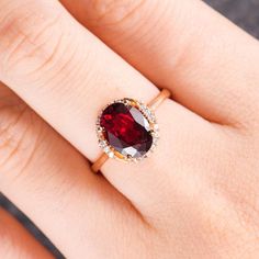 a woman's hand wearing a ring with a red stone in the middle and white diamonds around it