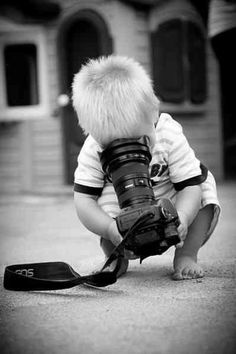 a small child with a camera and a bird on the ground in front of him