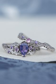 two silver rings with purple stones and leaves on the sides, sitting on top of a piece of paper