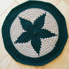 a crocheted blue and white round rug on the floor with an arrow in the center