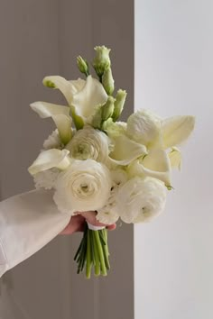 a bouquet of white flowers being held by a person's hand in front of a wall