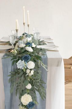 the table is set with blue and white flowers, greenery, candles and napkins