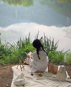 a woman sitting on top of a blanket next to a lake