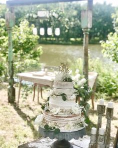 a wedding cake sitting on top of a table in front of a lake and greenery