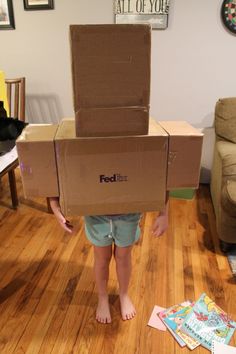 a young boy is standing on the floor with a box on his head