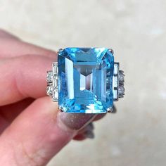 a person is holding an aqua ring with two diamonds on each side and the center stone surrounded by smaller blue stones