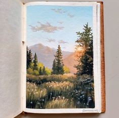 an open book with a painting of mountains and trees