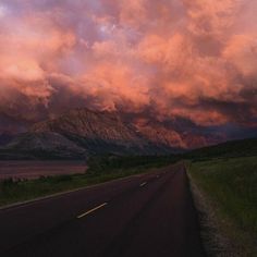 a long road with mountains in the distance under a cloudy sky at sunset or sunrise