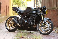 a black motorcycle parked on the side of a road next to a brick wall and trees