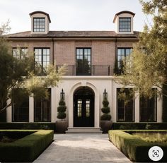 the front entrance to a large house with hedges and trees on either side of it