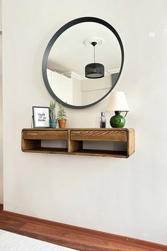 a mirror hanging on the wall next to a wooden shelf with two plants and a lamp