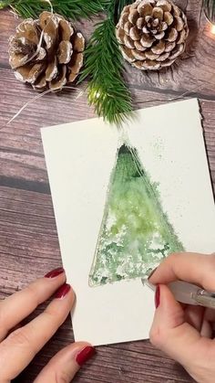 someone is painting a christmas tree with watercolors and pine cones on the table