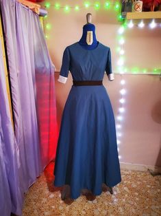 a blue dress on display in front of some colorful lights and drapes with curtains behind it