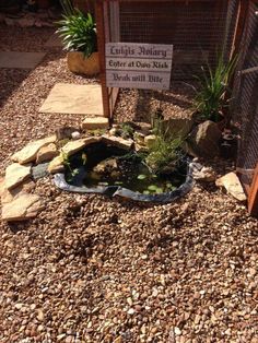 a small pond in the middle of a graveled area next to a fence and sign