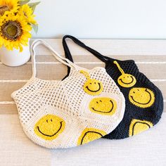 two crocheted smiley face bags sitting next to a vase with sunflowers