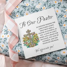 a card that is laying on top of a pillow with a cross and flowers around it