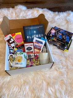 a box filled with books and coffee sitting on top of a fluffy white blanket next to a candle