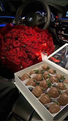 two boxes filled with chocolate covered strawberries next to a bouquet of roses and a car steering wheel