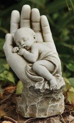 a statue of a hand holding a baby in it's palm on the ground