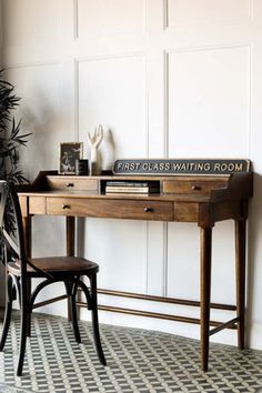 a wooden desk with a sign on it next to a chair and potted plant