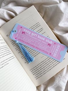 an open book with a tassel on top of it next to a pink and blue bookmark